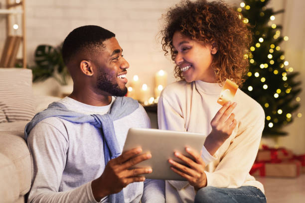 vorbereitung auf weihnachten. aufgeregt afro paar geschenke online kaufen - christmas shopping internet family stock-fotos und bilder