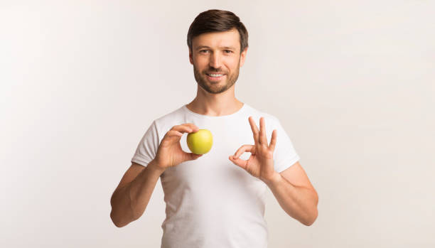 istock Man Holding Apple Gesturing OK Standing Over White Background 1186284128