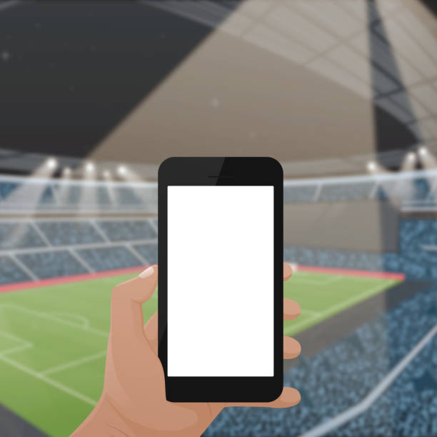istock Hand holding mockup mobile phone with white screen in the front of blurred football stadium. 1186285098