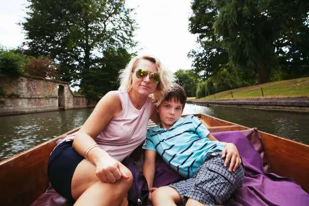 Cambridge, United Kingdom - August 22, 2016: beautiful mother and handsome boy are sitting close to each other and looking at camera in a canal in a boat.