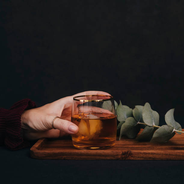 Woman drinking drink brandy whiskey or rum on ice\nClose up of hands and glass of alcohol