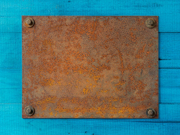 Old blank rusty steel metal plate sign bolted to an old weathered turquoise wooden fence wall. A blank rusty and weathered steel metal sign bolted by four bolts to a turquoise colored wooden paneled fence. Good copy space in the center of the metal plate. rusty fence stock pictures, royalty-free photos & images