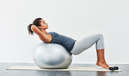Shot of a young woman exercising using a fitness ball