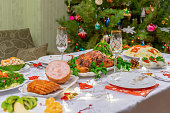 Festive Christmas served table against beautiful green pine tree decorated with many colorful new year toys. Xmas dinner, delicious food, christmas turkey. Winter holidays celebration at cozy home