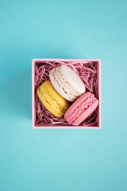 istock Beige, yellow and pink macaroons in pink box with decorative pink elements on a mint color background. Flat lay. 1186293540