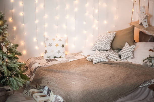 istock Rustic bedroom interior decorated for Christmas. New Year's interior Scandinavian style bed with pillows. Textural light room of a farmer's house with a Christmas tree and a garland. Background for text. 1186300061