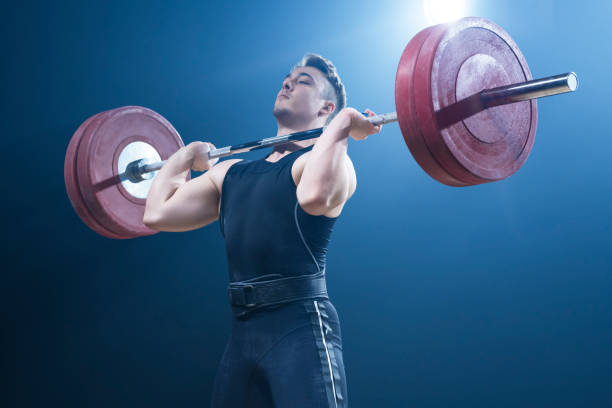 Male weightlifter performing clean and jerk lift Young male weightlifter lifting barbell while performing clean and jerk lift. clean and jerk stock pictures, royalty-free photos & images