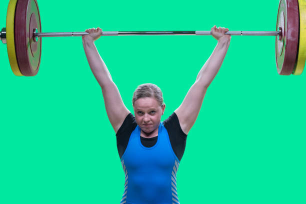 Female weightlifter performing clean and jerk lift Portrait of young female weightlifter lifting barbell above her head while performing clean and jerk lift. clean and jerk stock pictures, royalty-free photos & images