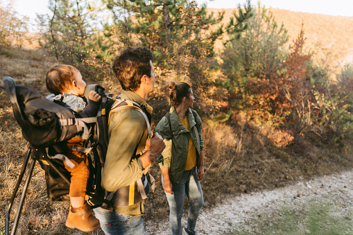 Photo of young family hiking with their toddler son while he is in a baby carrier backpack