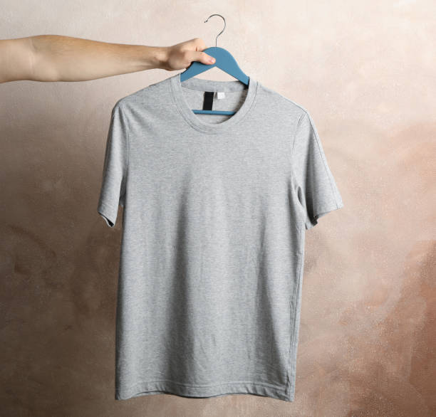 istock Man holds a hanger with blank gray t-shirt on brown background, space for text 1186302003