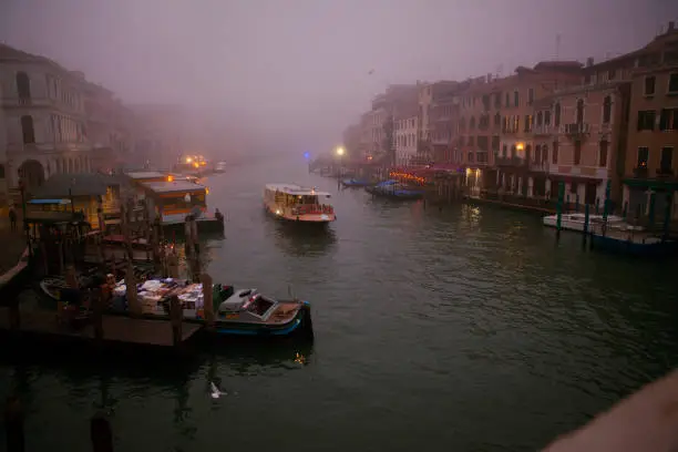 Venice. Italy - October 28, 2019: first vaporetto is making its way on the Grand Canal in Venice in the misty autumn morning among other empty boats, seen from Rialto bridge.