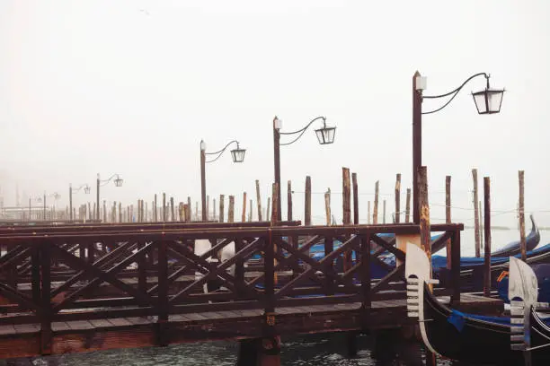 Venice, Italy - October 28, 2019: no people on wooden piers where Venice famous gondolas are parked and waiting for the tourists. It's a very early fall autumn without sun only with mist. Beautiful geometrical shapes.