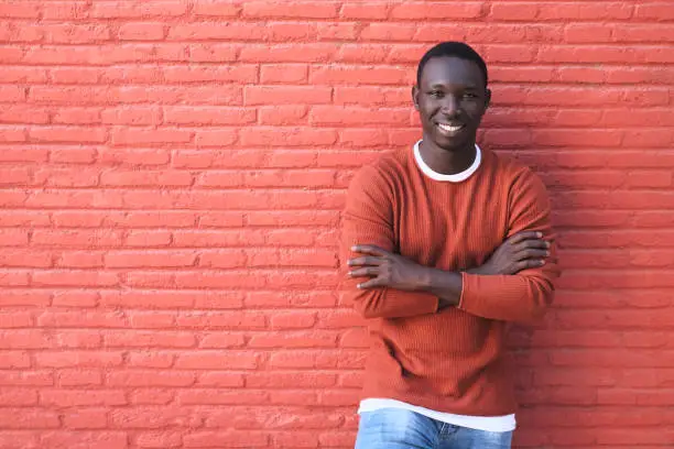 Portrait Of African Young Man Looking At Camera And Smiling. Copy Space On Red Wall In Background.