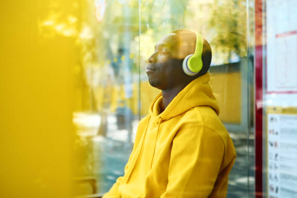 afrikanischer junger mann hört musik an bushaltestelle - bussing stock-fotos und bilder