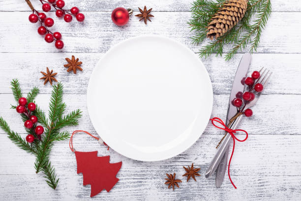 Christmas table place setting with empty white plate, cutlery with festive decorations on wooden background