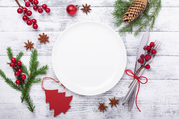 Christmas table place setting with empty white plate, cutlery with festive decorations on wooden background stock photo