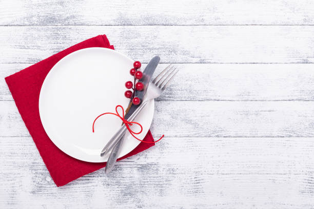 Christmas table place setting with empty white plate, cutlery with festive decorations on wooden background stock photo