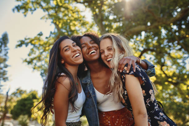 Portrait of a happy multiethnic group of smiling female friends - women laughing and having fun in the park on a sunny day Cheerful excited positive modern group of female friends hugging together in park and laughing and having fun friendly smile stock pictures, royalty-free photos & images