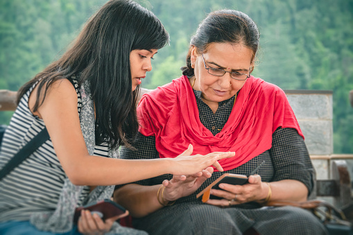 An Asian/Indian beautiful daughter teaches the smartphone operating to her senior retired mother at a resort in the mountains of Himachal Pradesh.