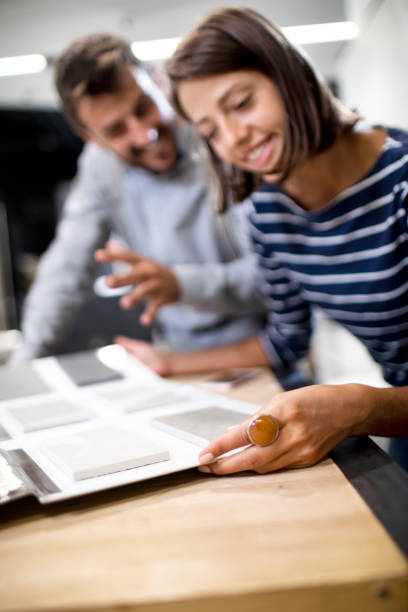 deux jeunes acheteurs ayant une discussion tout en regardant des échantillons d'échantillon de tuile dans un catalogue - rectangle redecorate photos et images de collection