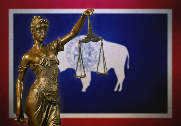 Close-up of a small bronze statuette of Lady Justice before a flag of Wyoming.