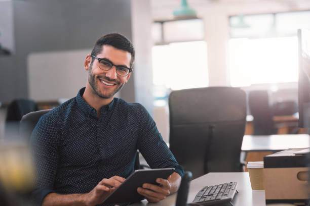 istock Smiling young businessman using a tablet at his office desk 1186332583