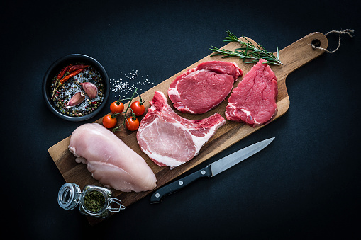 Surtido de carne cruda - Chuletas de carne de res, pollo y cerdo rodadas desde arriba sobre fondo oscuro photo