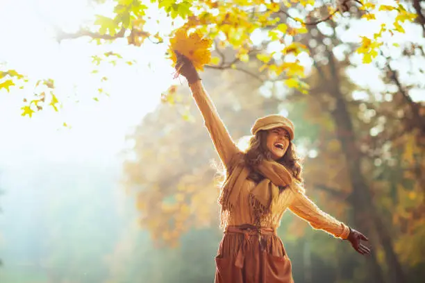Hello autumn. carefree trendy woman in sweater, skirt, hat, gloves and scarf with yellow leaves having fun time outside in the autumn park.