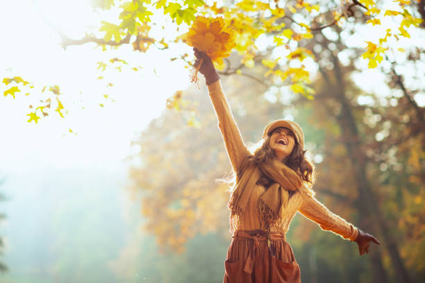 mujer feliz con hojas amarillas regocijándose al aire libre en el parque de otoño - autumn glory fotografías e imágenes de stock