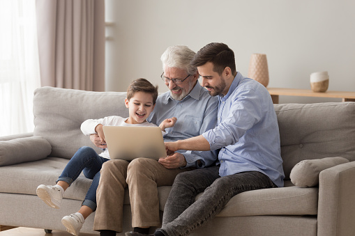 Happy three 3 age multi generation men family old grandfather young adult grown son father and child boy grandson having fun using laptop computer spend time browsing internet at home sit on sofa