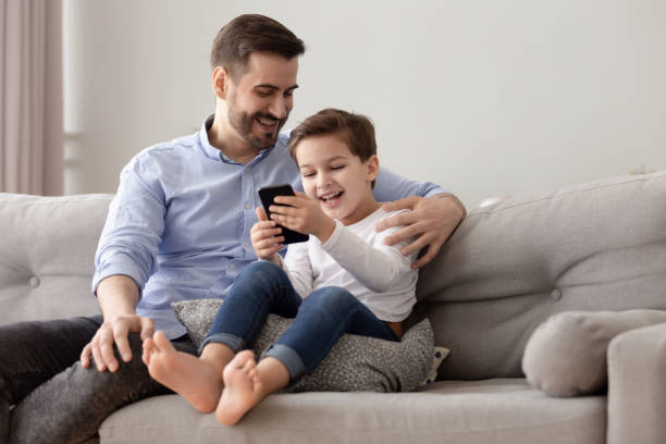 istock Happy dad and child son relaxing on sofa using phone 1186336098