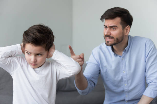 Angry father shouting at stubborn fussy little son closing ears Angry mad father shouting at stubborn fussy little kid son close ears not listening ignoring dad punish rebellious kid boy for bad behavior, parents and children family conflicts arguments concept scolding stock pictures, royalty-free photos & images