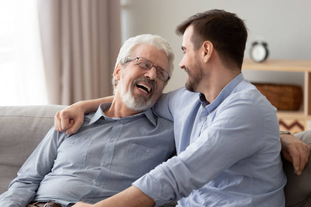 Happy two generations male family laugh talking bonding on sofa Happy two generations male family laugh enjoy talking bonding embracing sit on sofa at home, old senior father and young adult grown son relaxing having fun hugging chatting on couch on fathers day father son grandfather fathers day stock pictures, royalty-free photos & images