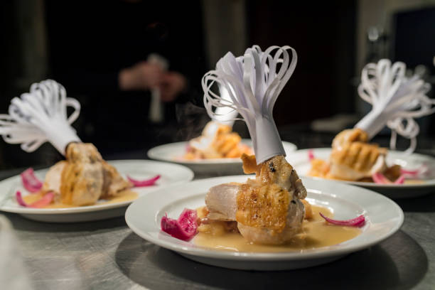 Dish of guinea fowl with apple and bacon at the pass. Plates of guinea fowl with pan-fried apple and bacon at the pass, waiting ready to be served in the restaurant. Colour, horizontal with some copy space, photographed on location at a restaurant on the island of Moen in Denmark. guinea fowl stock pictures, royalty-free photos & images