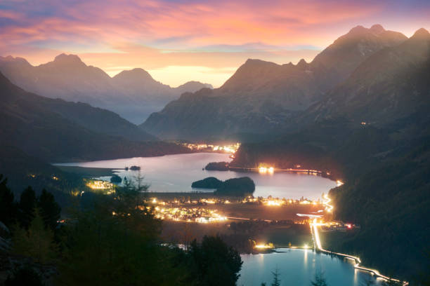 Silvaplana in Switzerland is a beautiful chain of lakes surrounded by picturesque rocky peaks. The starry sky of the Galaxy and the lights of cities and villages below are beautiful