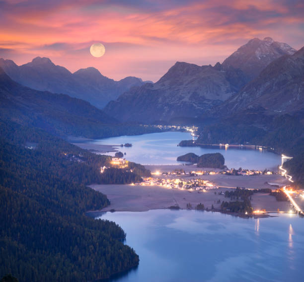 Panorama of the night Silvaplan. Silvaplana in Switzerland is a beautiful chain of lakes surrounded by picturesque rocky peaks. The starry sky of the Galaxy and the lights of cities and villages below are beautiful graubunden canton stock pictures, royalty-free photos & images