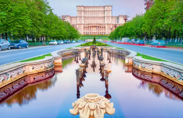Stock photograph of fountains along the tree-lined Bulevardul Unirii, a major thoroughfare in central Bucharest, with the Palace of the Parliament in the background at dawn.