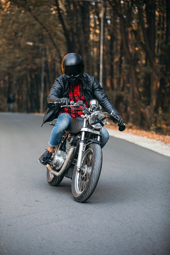 Young man driving custom made motorcycle in a leather jacket.