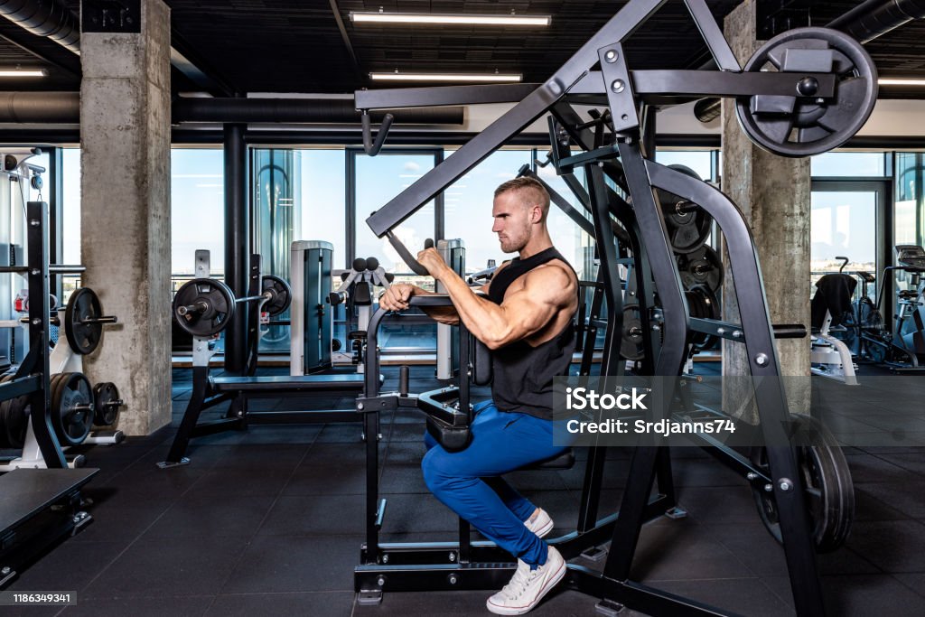 Joven sudoroso fuerte muscular ajuste hombre back muscles entrenamiento entrenamiento con pesas en la máquina en el gimnasio - Foto de stock de 20 a 29 años libre de derechos Joven sudoroso fuerte muscular ajuste hombre back muscles entrenamiento entrenamiento con pesas en la máquina en el gimnasio - Foto de stock de 20 a 29 años libre de derechos