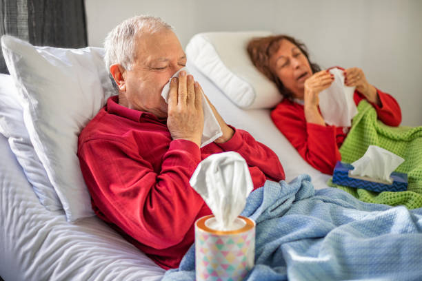 coppia di anziani sdraiati sul letto e soffiare il naso - cold and flu flu virus bed couple foto e immagini stock