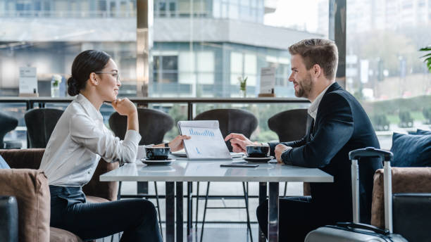 Two business people sitting in modern airport building with documents to discuss