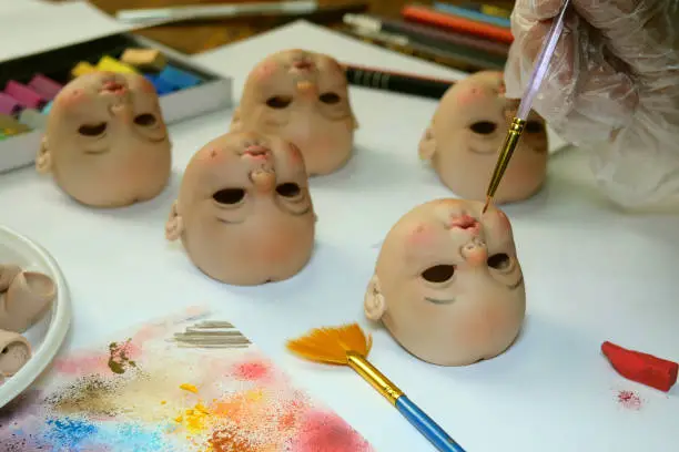 Photo of Making dolls. Master painter carefully paints lips of blank for doll with thin brush. Concept of combining work and hobbies.