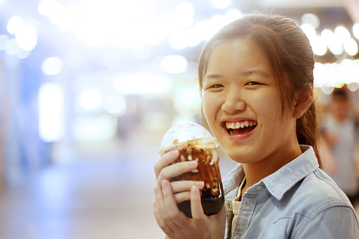 One teenage girl is holding a cup of boba (tapioca pearl bubble) cooked with brown sugar, added ice cubes, fresh milk and topped with burnt pearlised brown sugar, cheerfuly.