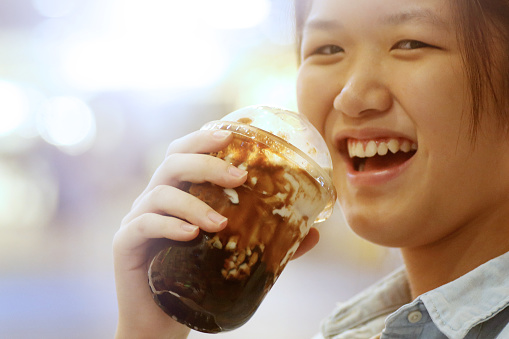 One teenage girl is holding a cup of boba (tapioca pearl bubble) cooked with brown sugar, added ice cubes, fresh milk and topped with burnt pearlised brown sugar, cheerfully.