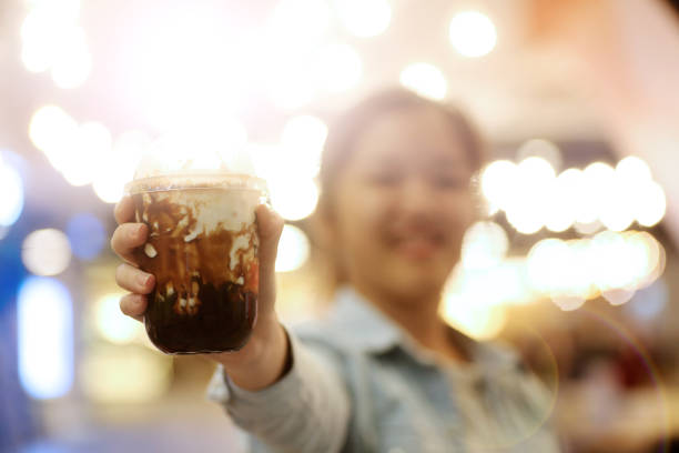 One teenage girl is holding a cup of boba (tapioca pearl bubble) cooked with brown sugar, added ice cubes, fresh milk and topped with burnt pearlised brown sugar, cheerfully.