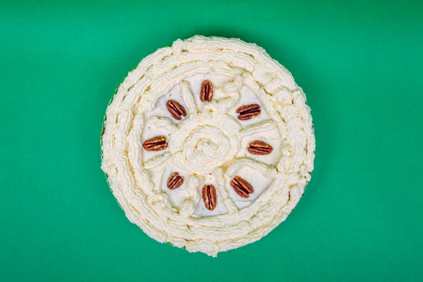 Top view round carrot cake with creamy frosting decorated with walnuts on a green background
