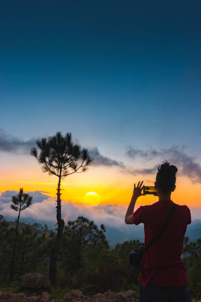 Kobieta strzela pochmurny widok zachodu słońca w górach za pośrednictwem smartfona. – zdjęcie