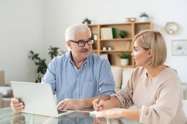 istock Young woman making notes in notepad while looking at senior father with laptop 1186371578