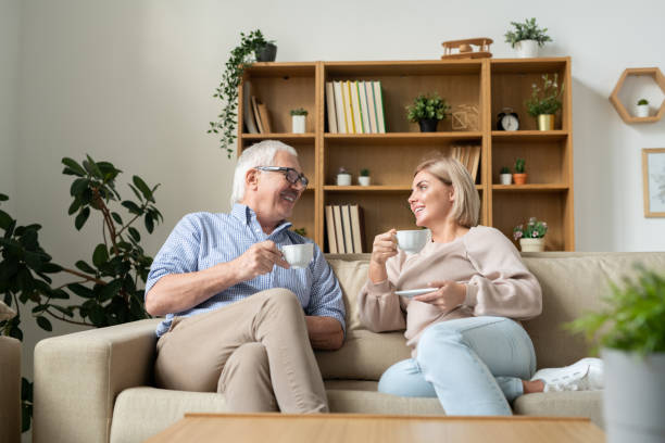 istock Happy female and her senior father having tea while sitting on couch and talking 1186371591