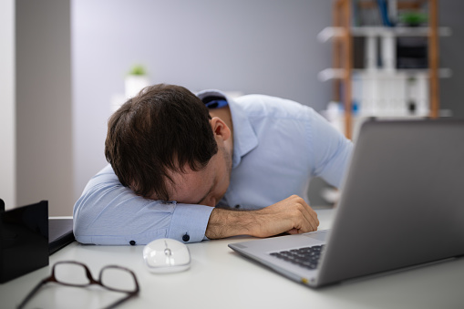 Young Businessman With Laptop Sleeping At Desk In Office
